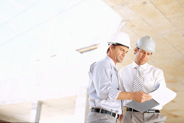 Two foremen looking at plans inside a white building under construction