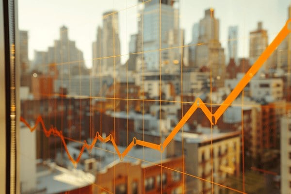 An orange line graph mapped across an office window with a downtown view behind it