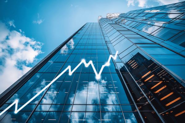 An upward view of a skyscraper against a blue sky with an increasing line graph mapped across the windows