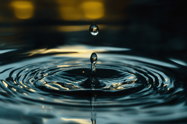 A close-up image of a droplet of water hitting a water surface, causing ripples