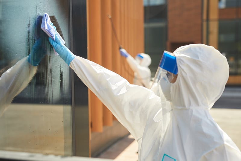 Two people wearing hazmat suits and cleaning a building