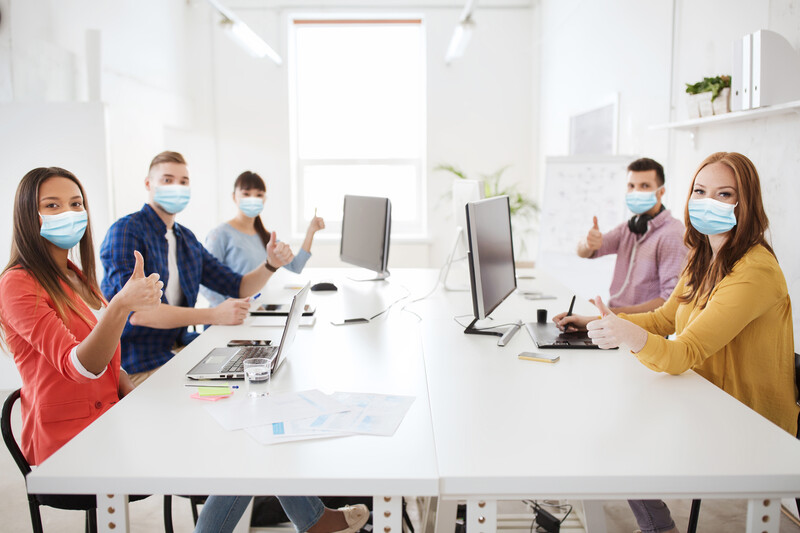 Five business people sitting in an office meeting wearing medical masks