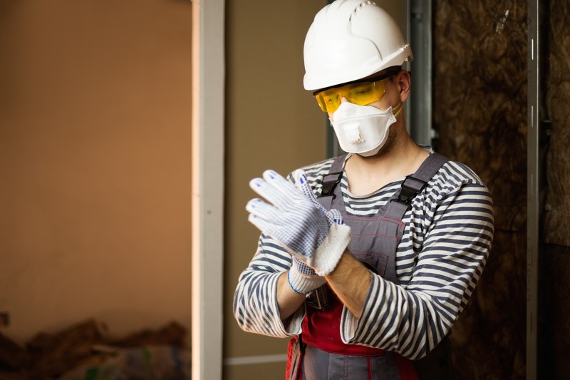 Construction worker with mask and helmet putting work gloves on
