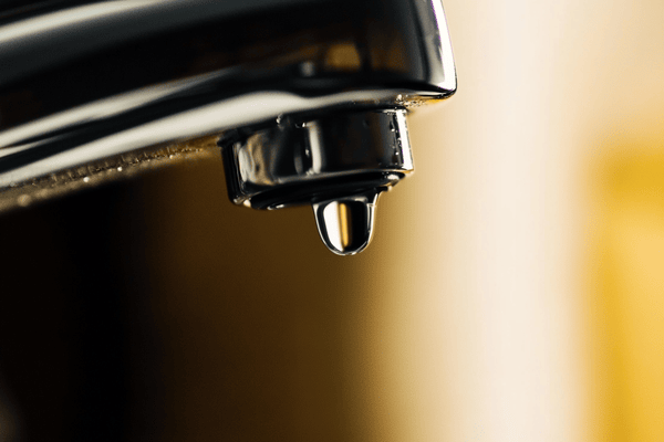 A close-up image of a drop of water about to fall from a faucet into a sink