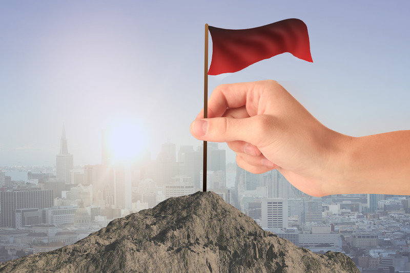 Hand putting red flag on mountain in front of cityscape