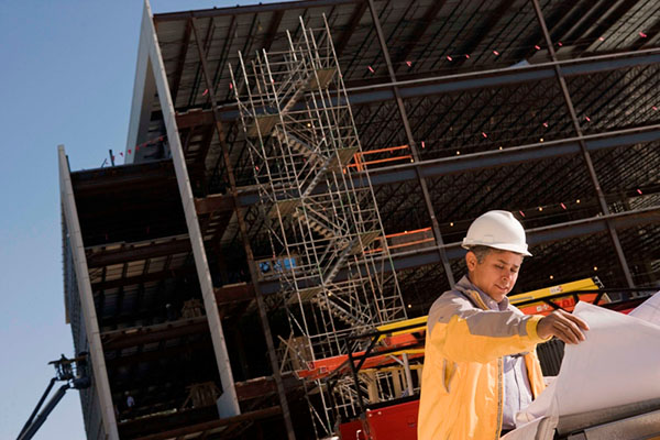 A construction worker looking at blueprint with  building under construction in background