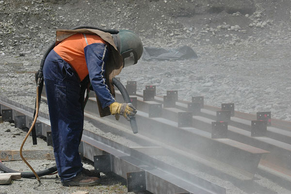 Construction worker sandblasting beams