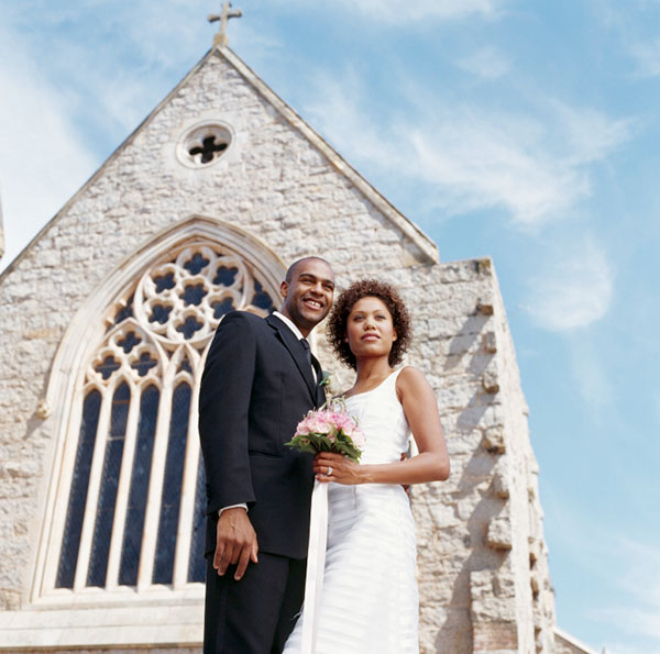 Woman in wedding gown holding bouqet and man in tuxedo in front of church