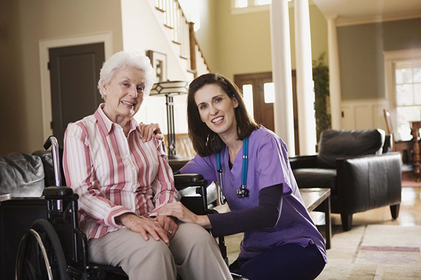 A kneeling nurse next to an old woman in a wheelchair
