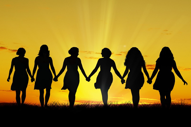 6 women holding hands and walking toward sunset