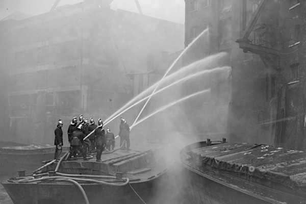 Black and white photo of firefighters spraying building with water