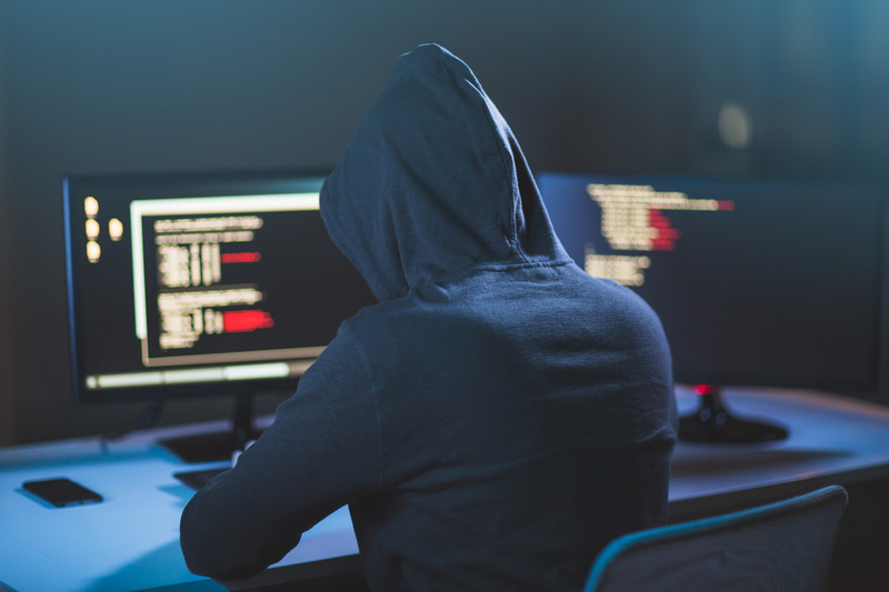 Malicious hacker from behind in a hoodie using a computer