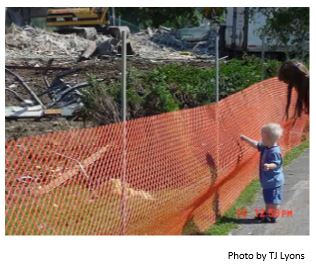 Child standing behind an orange fence in front of a construction site