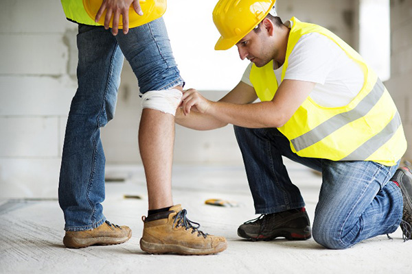 Construction worker putting a brace on another worker's knee