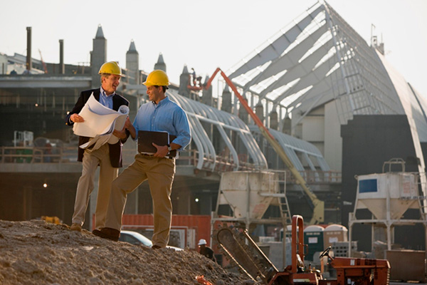 Two foremen looking at plans with construction site in background