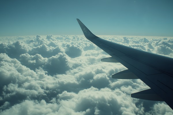 An airplane wing seen stretching out from the airplane window with blue sky and clouds beneath it