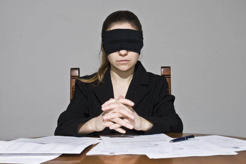 Woman in blindfold sitting behind desk covered with papers