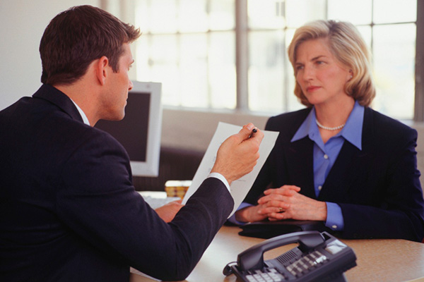 Man in suit interviewing woman in suit at desk