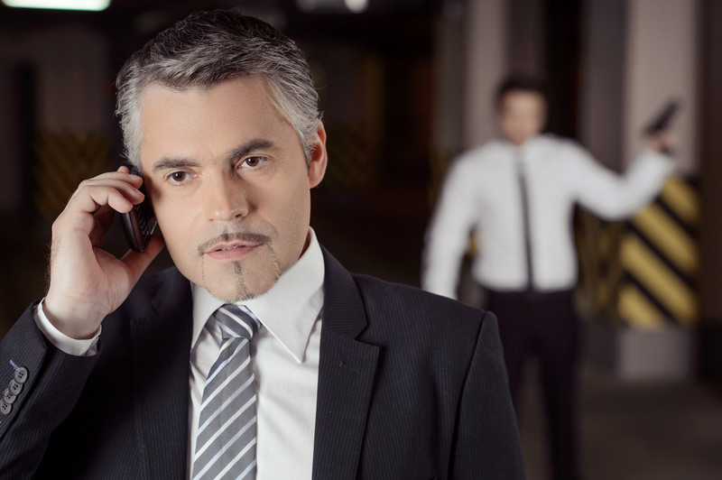 Businessman on phone--man with gun blurry in background