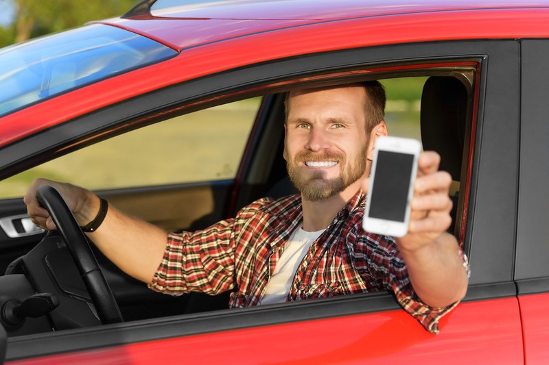 Smiling man in red car holding cell phone out