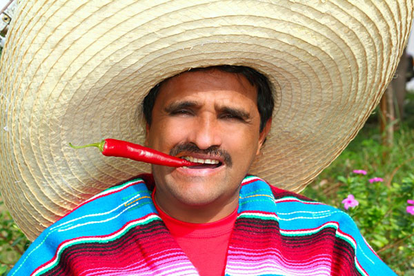 Man in poncho and sombrero eating red hot chili