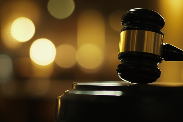 A close-up image of a wooden gavel with gold wrapped around the middle