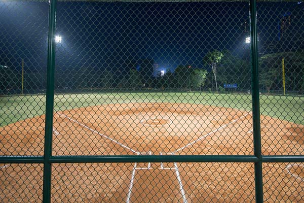 An empty baseball field at night as seen through a chainlink fence