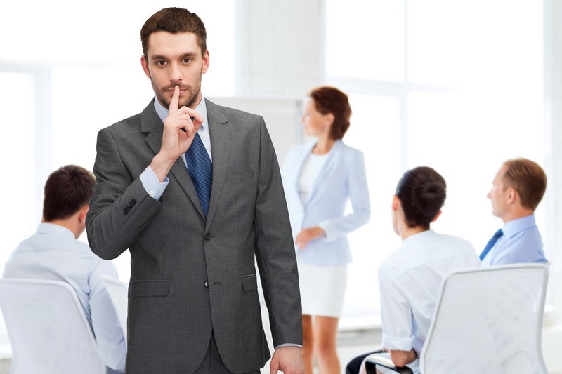 Businessman with finger to lips in front of blurry meeting