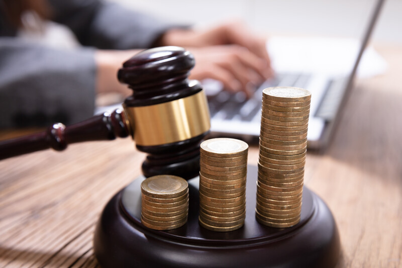 Hands typing on a laptop in background with gavel and a rising stack of coins