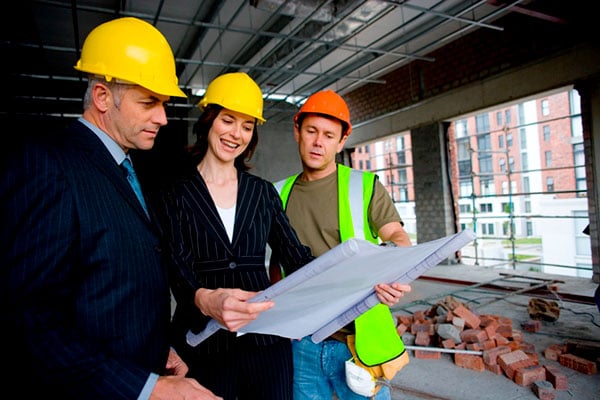 A man and a woman in suits looking at plans with a construction worker at a worksite