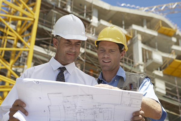 An architect and contractor going over blueprints together in front of a large building under construction