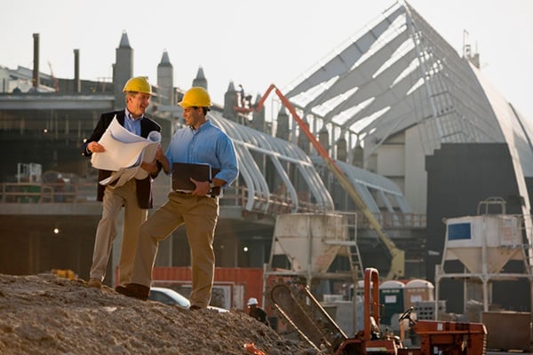 Two foremen looking at plans with construction site in background