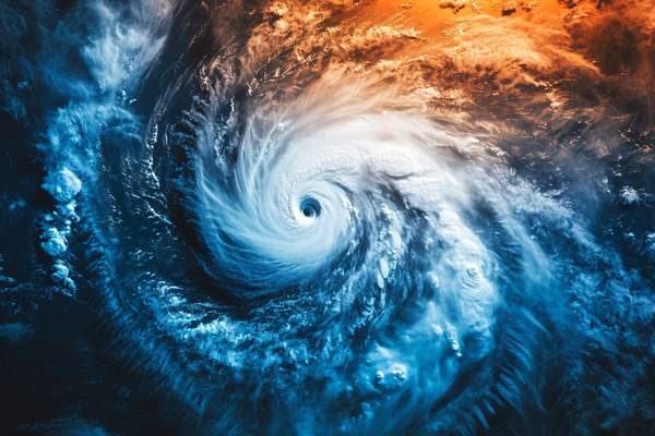 An aerial view of a hurricane and its eye with outer clouds glowing with blues and oranges