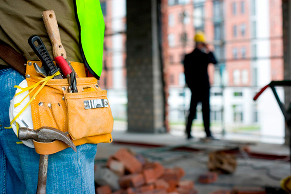 A construction worker wearing a tool belt's backside and a man wearing a suit talking on phone on right